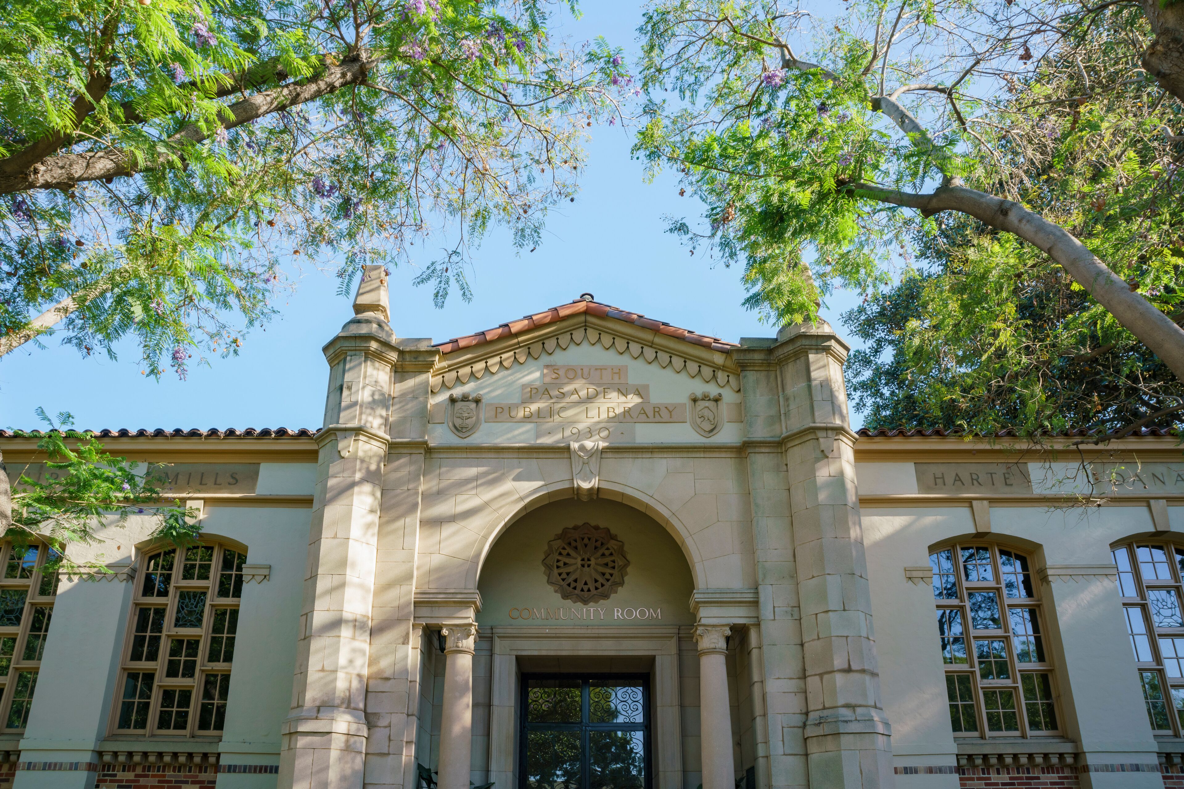 The South Pasadena Public Library entrance with a community room sign, surrounded by trees.