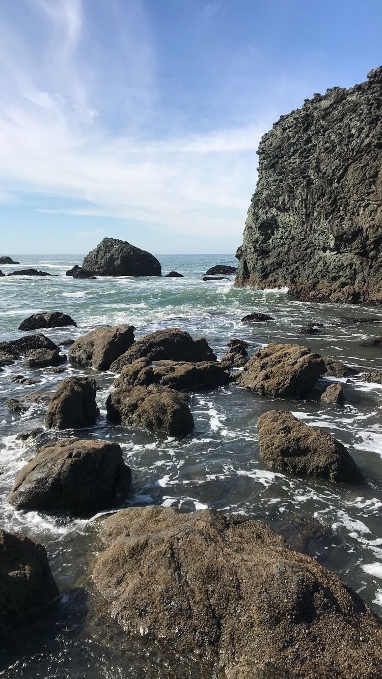 A rocky coastline with waves crashing against large boulders and a steep cliff.