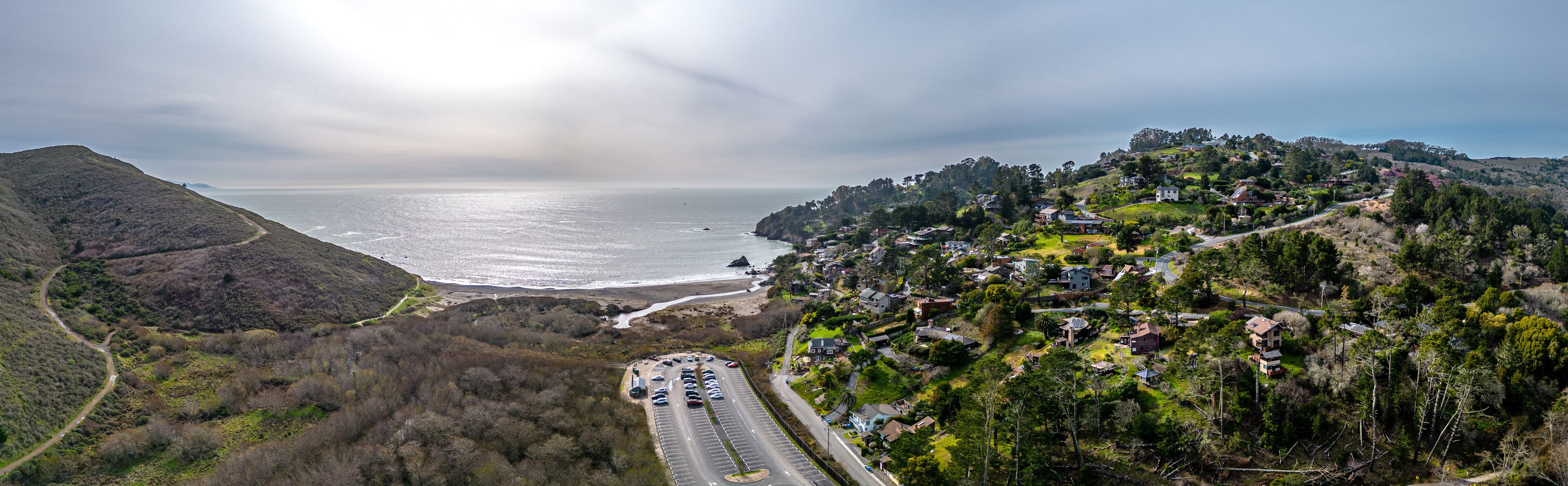 A coastal road with houses on a hillside, overlooking the ocean.