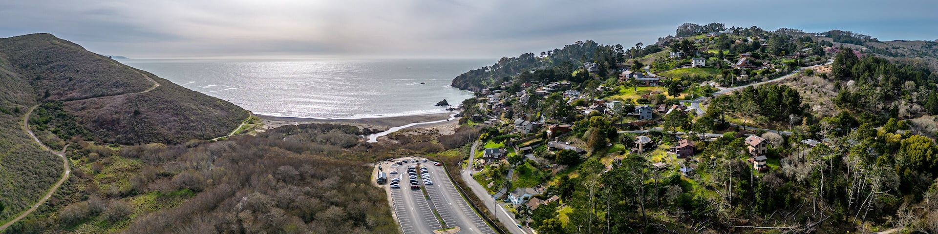 A coastal road with houses on a hillside, overlooking the ocean.