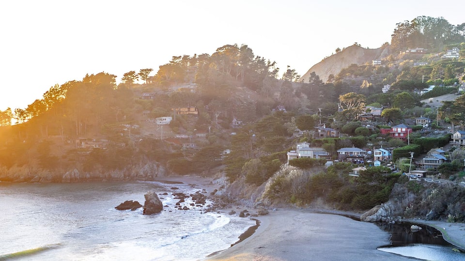 A coastal landscape with a beach, rocky shoreline, and houses on a hillside.