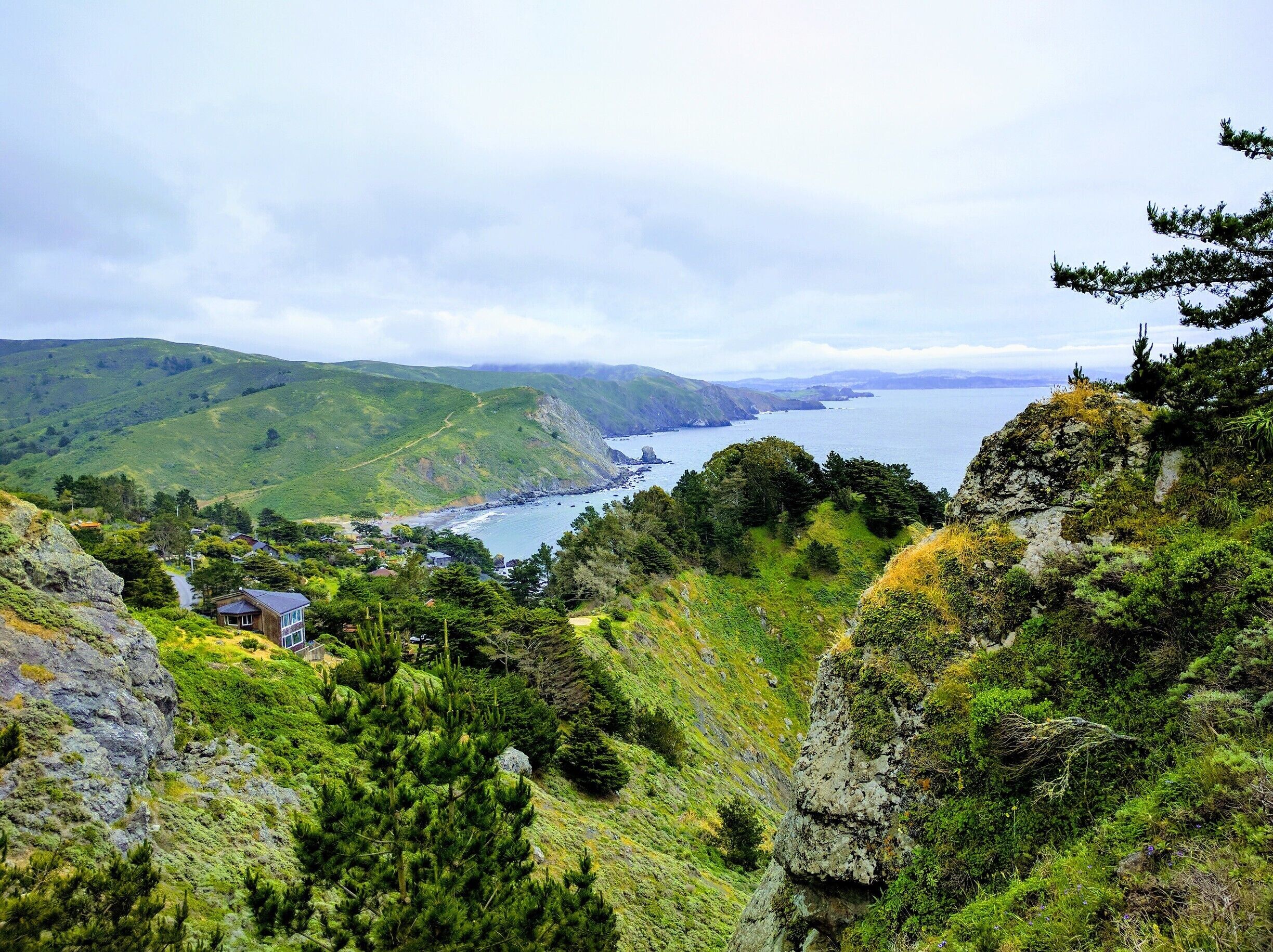 A coastal landscape with green hills, a rocky shoreline, and a small house.