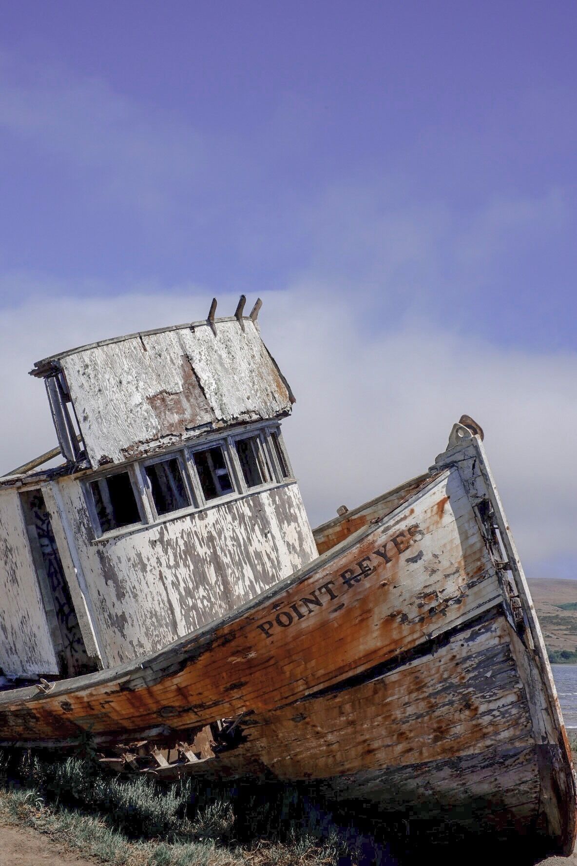 A rusted, abandoned ship with the name "POINT REYES" on its side, lying on a beach with a clear sky in the background.