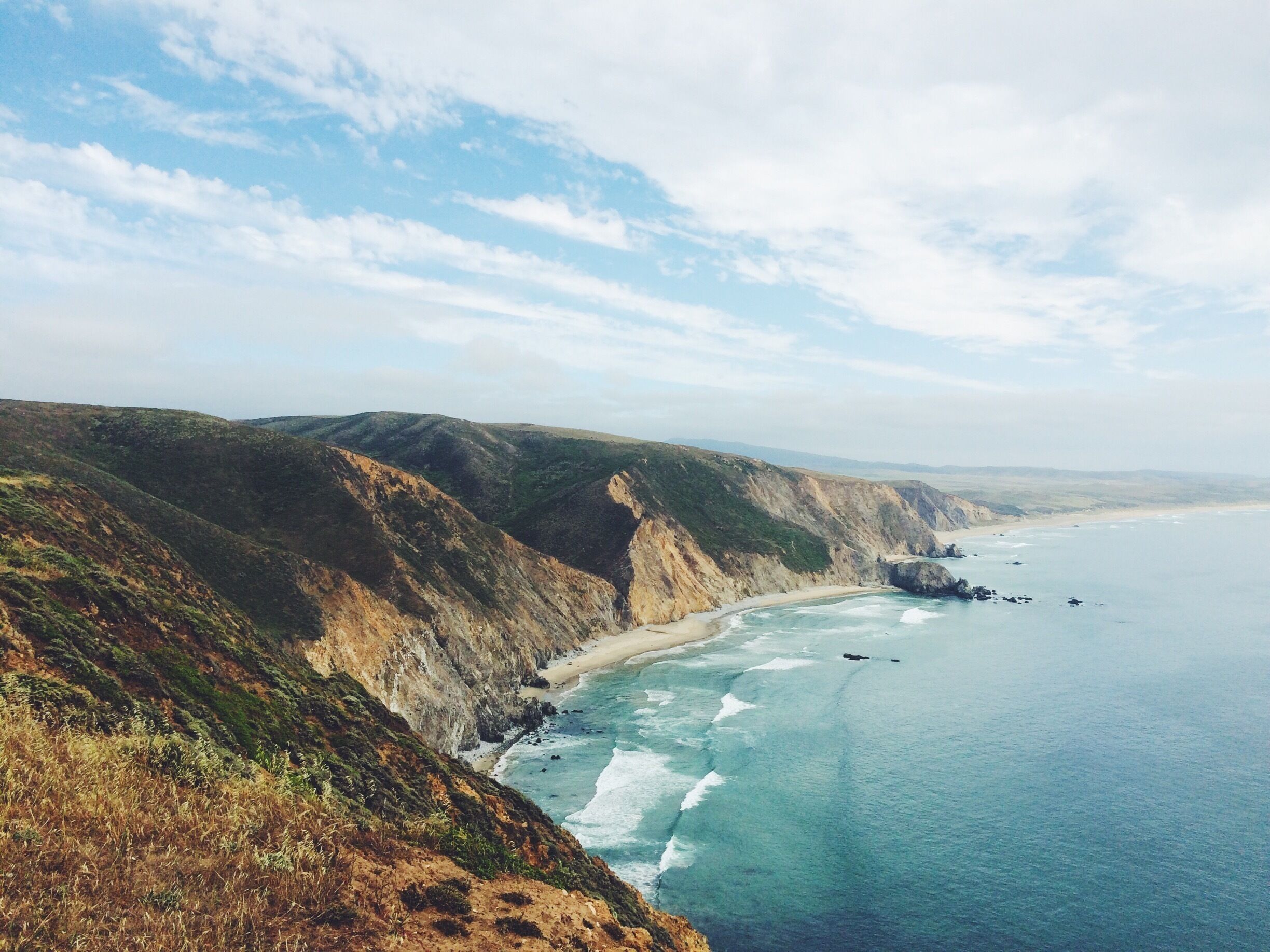 A coastal landscape with cliffs, a sandy beach, and the ocean.