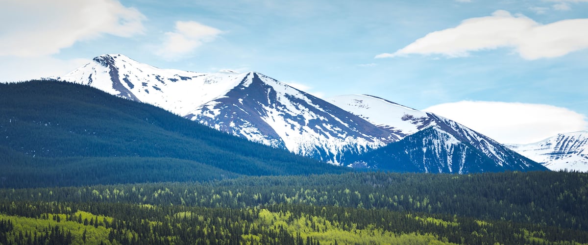 A snow-capped mountain range with dense forests at its base.