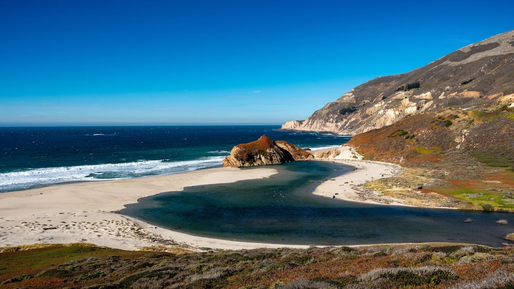 Dramatic seascape of little Sur River draining into the Pacific Ocean in Monterey bay with cliffs and waves breaking on the sandy beach. Off if highway 1.