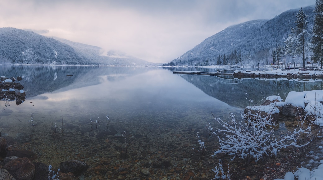Beautiful mountain and lake winter panorama landscape of calm reflection on Kootenay Lake with sunrise or sunset light and mist in Nelson, British Columbia, Canada.