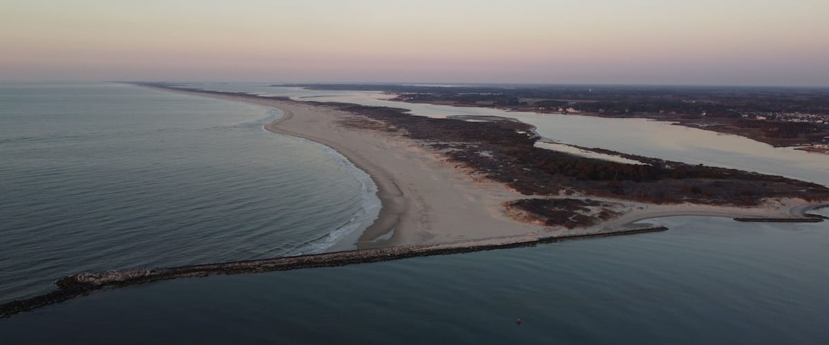 A coastal landscape with a sandy beach, a rocky barrier, and a calm sea.