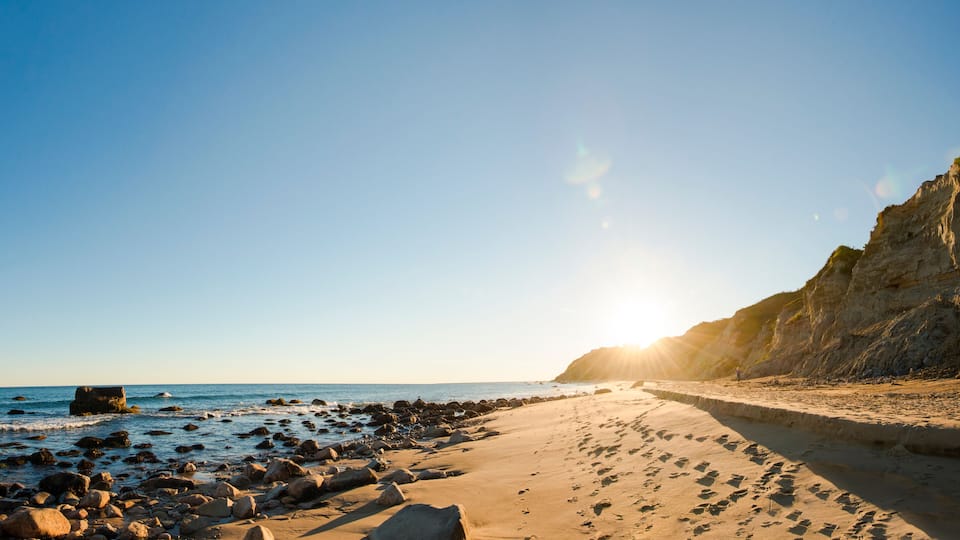 A sandy beach with rocky outcrops and a clear sky.
