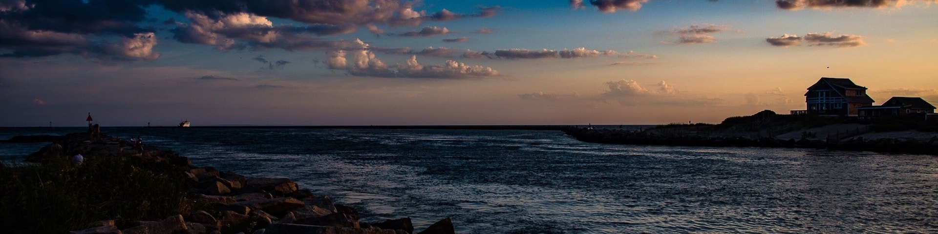A rocky shoreline with a house on a cliff overlooking the ocean at sunset.