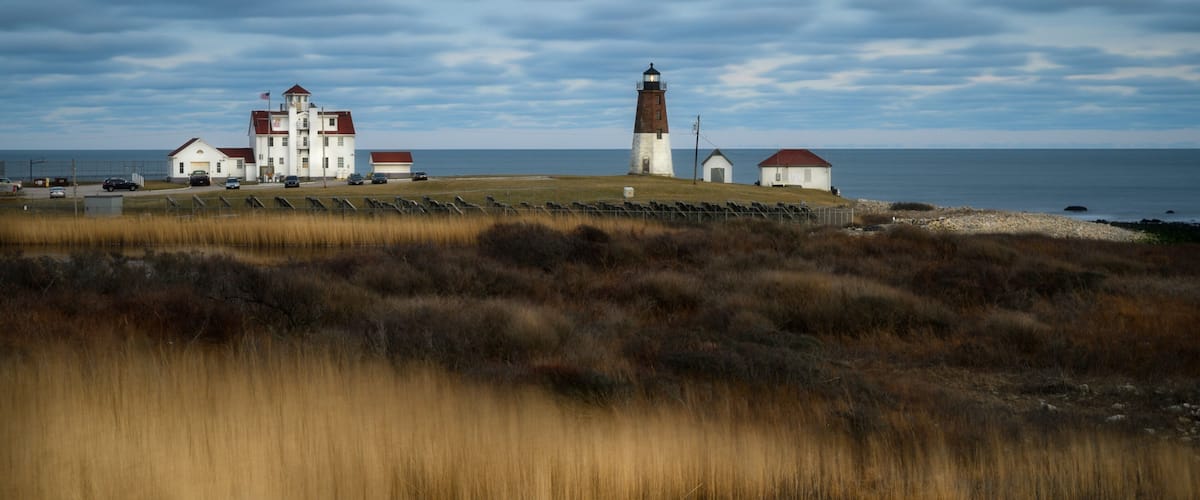 A coastal landscape with a lighthouse, a white building with a red roof, and a small red-roofed structure.