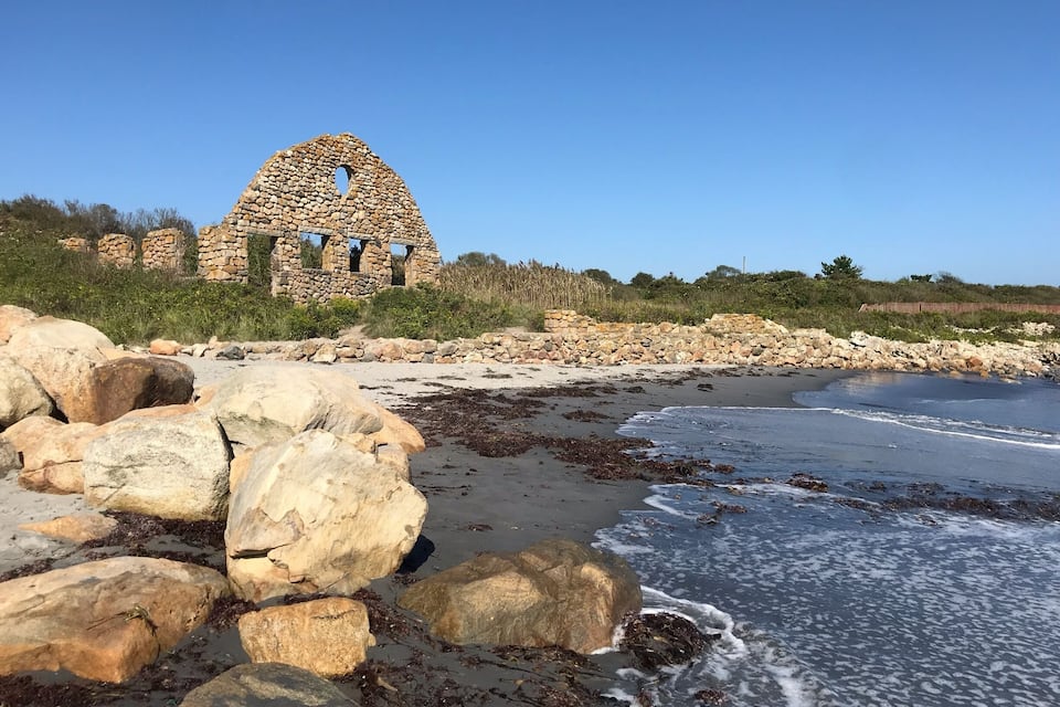 A stone structure with a circular opening on a beach with large rocks and seaweed.