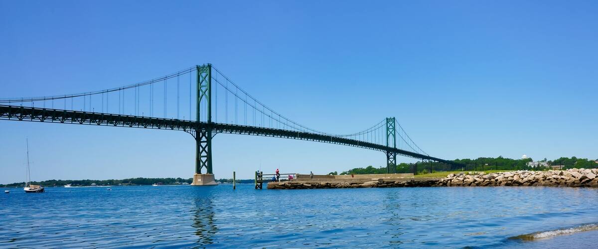 A large suspension bridge over a body of water with boats and a rocky shoreline.