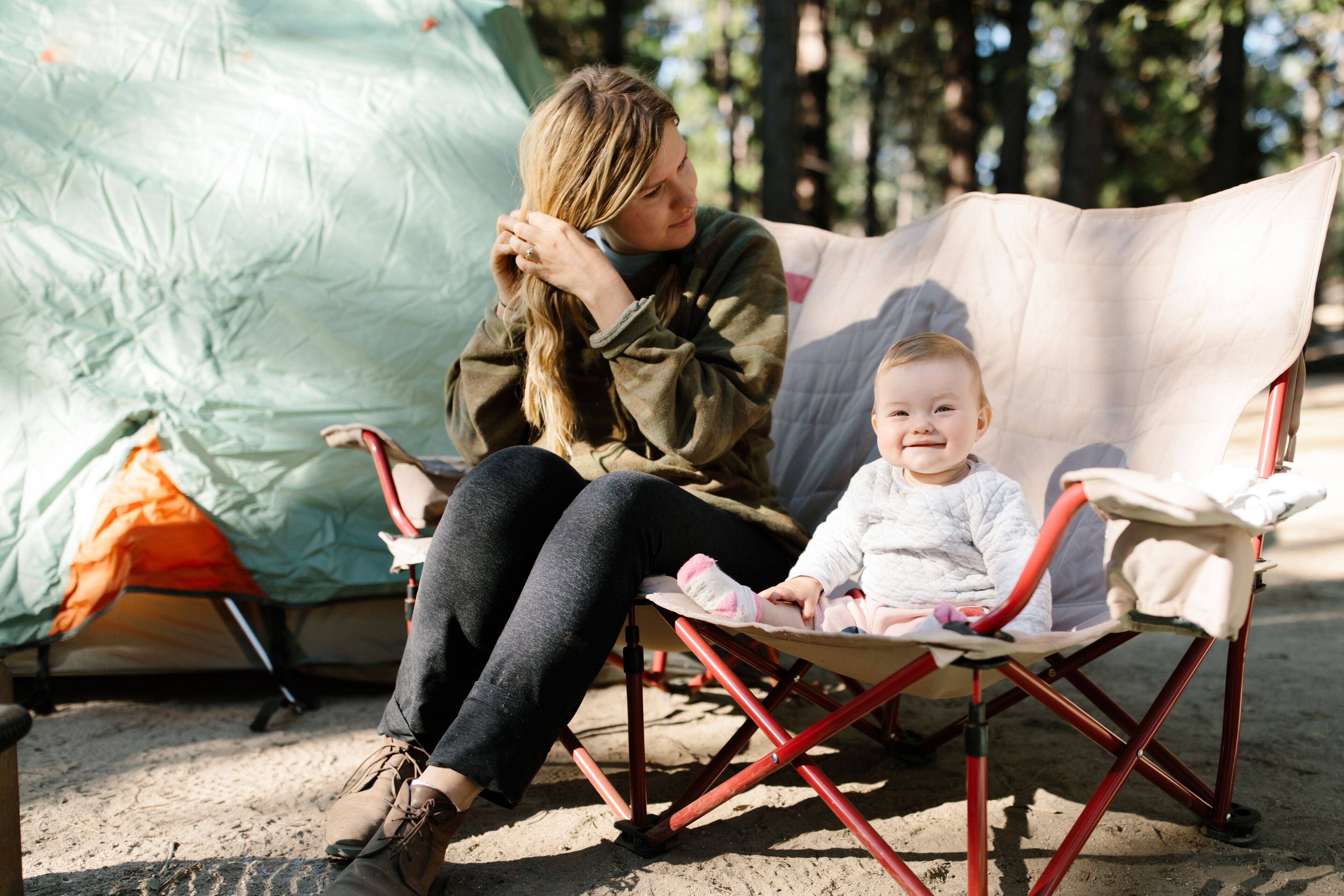 mother and her baby girl sitting on a camp chair outdoors while camping