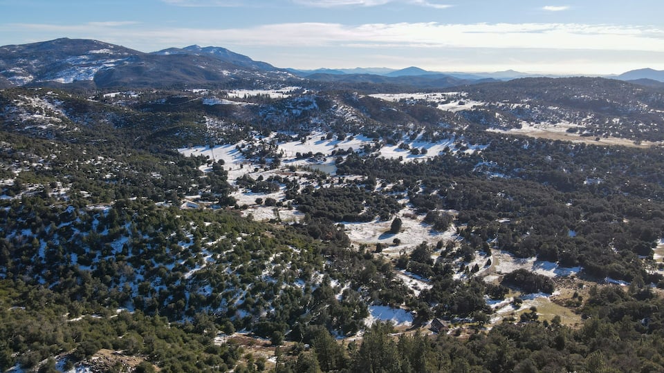 A mountainous landscape with scattered snow patches and dense forests.