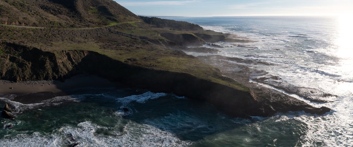 A coastal landscape with a rugged coastline, a winding road, and a beach.