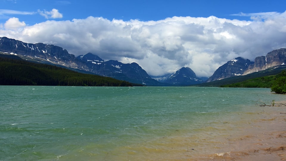 A lake surrounded by mountains with snow-capped peaks and dense forests.