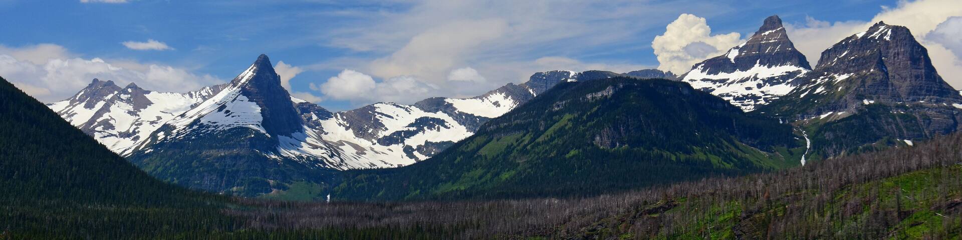 A mountain range with snow-capped peaks, a lake, and a forested valley.