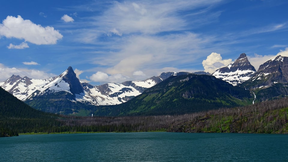 A mountain range with snow-capped peaks, a lake, and a forested valley.