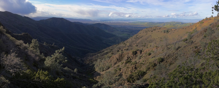 A valley with mountains, trees, and a distant cityscape.