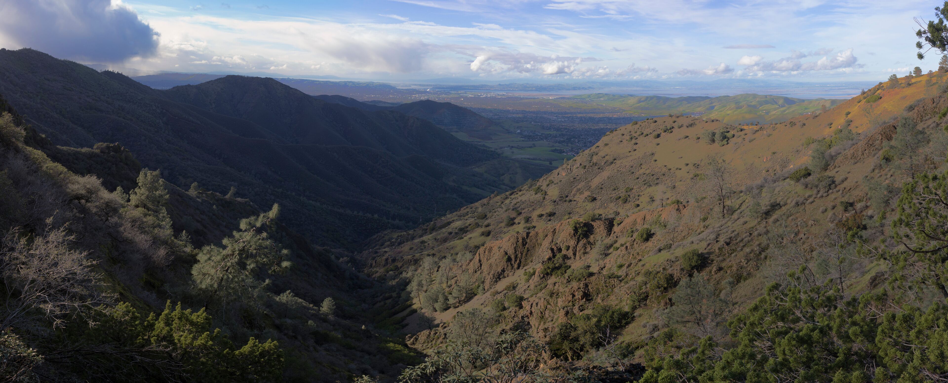 A valley with mountains, trees, and a distant cityscape.