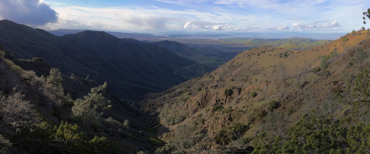 A valley with mountains, trees, and a distant cityscape.