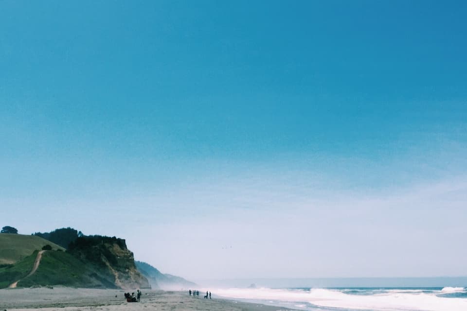 Une plage bordée d’une falaise rocheuse, avec des vagues déferlantes et un ciel dégagé.