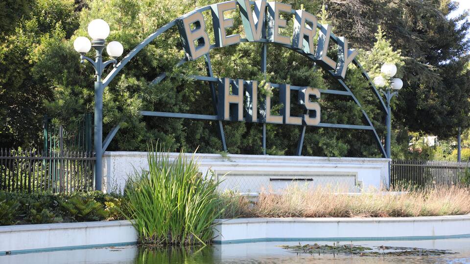 A sign with 'Beverly Hills' written on it, surrounded by greenery and a pond with ducks.