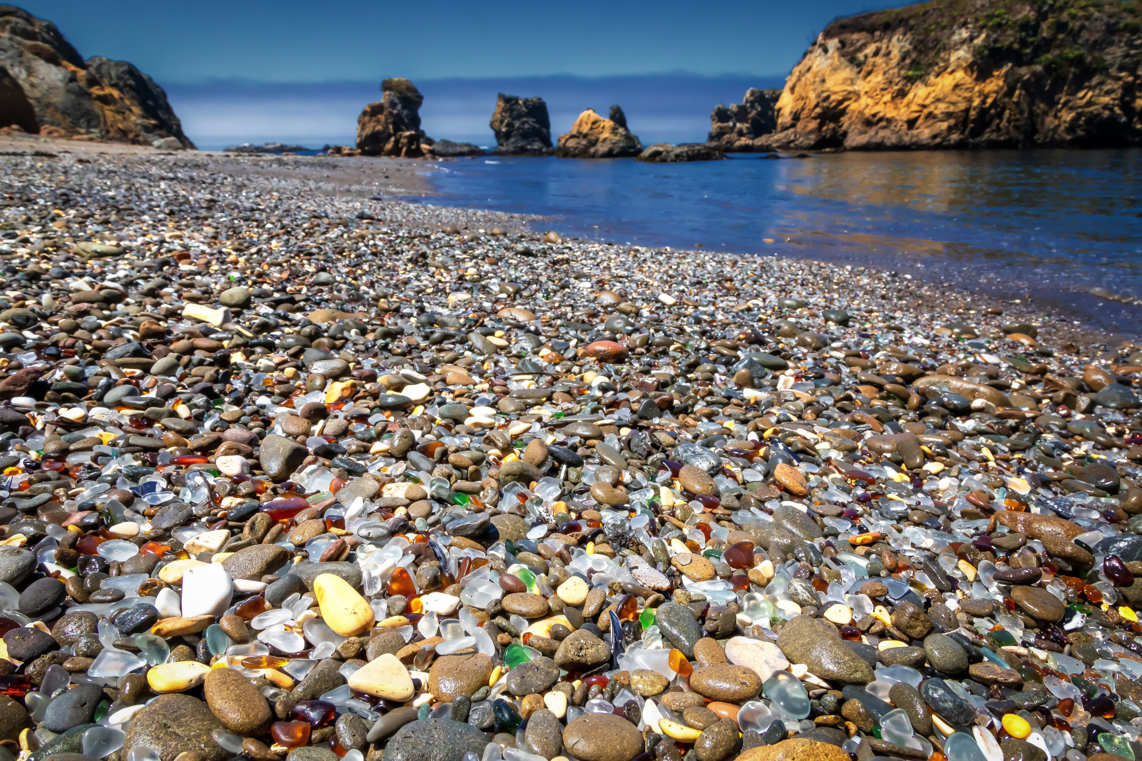 Una playa pedregosa con piedras variadas y acantilados rocosos al fondo.