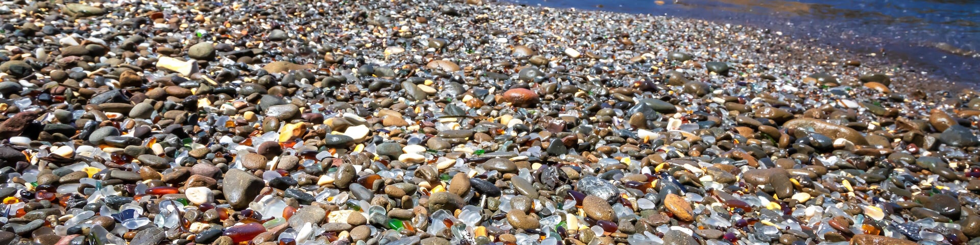 Una playa pedregosa con piedras variadas y acantilados rocosos al fondo.