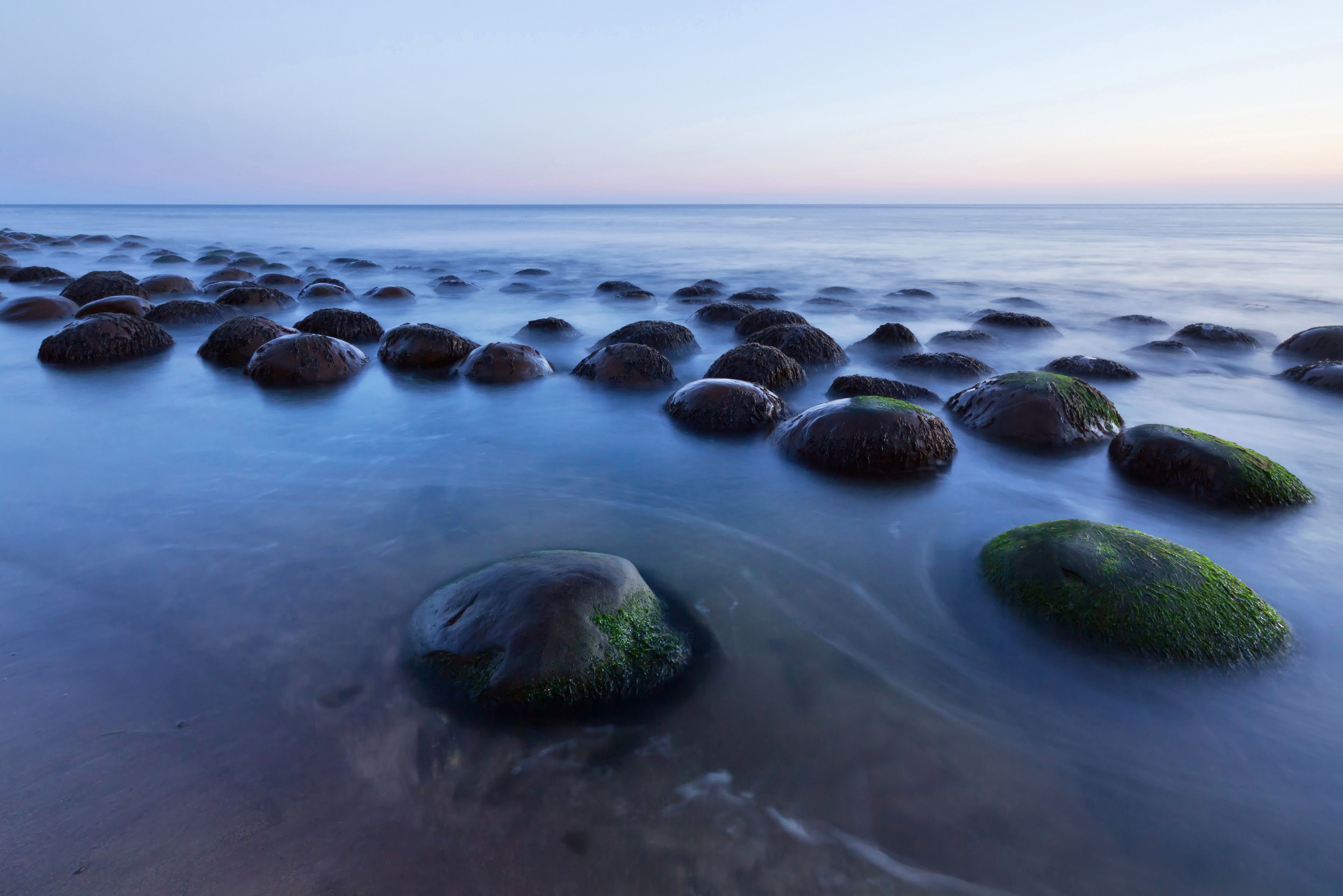 A beach with numerous smooth, rounded rocks and a calm sea.