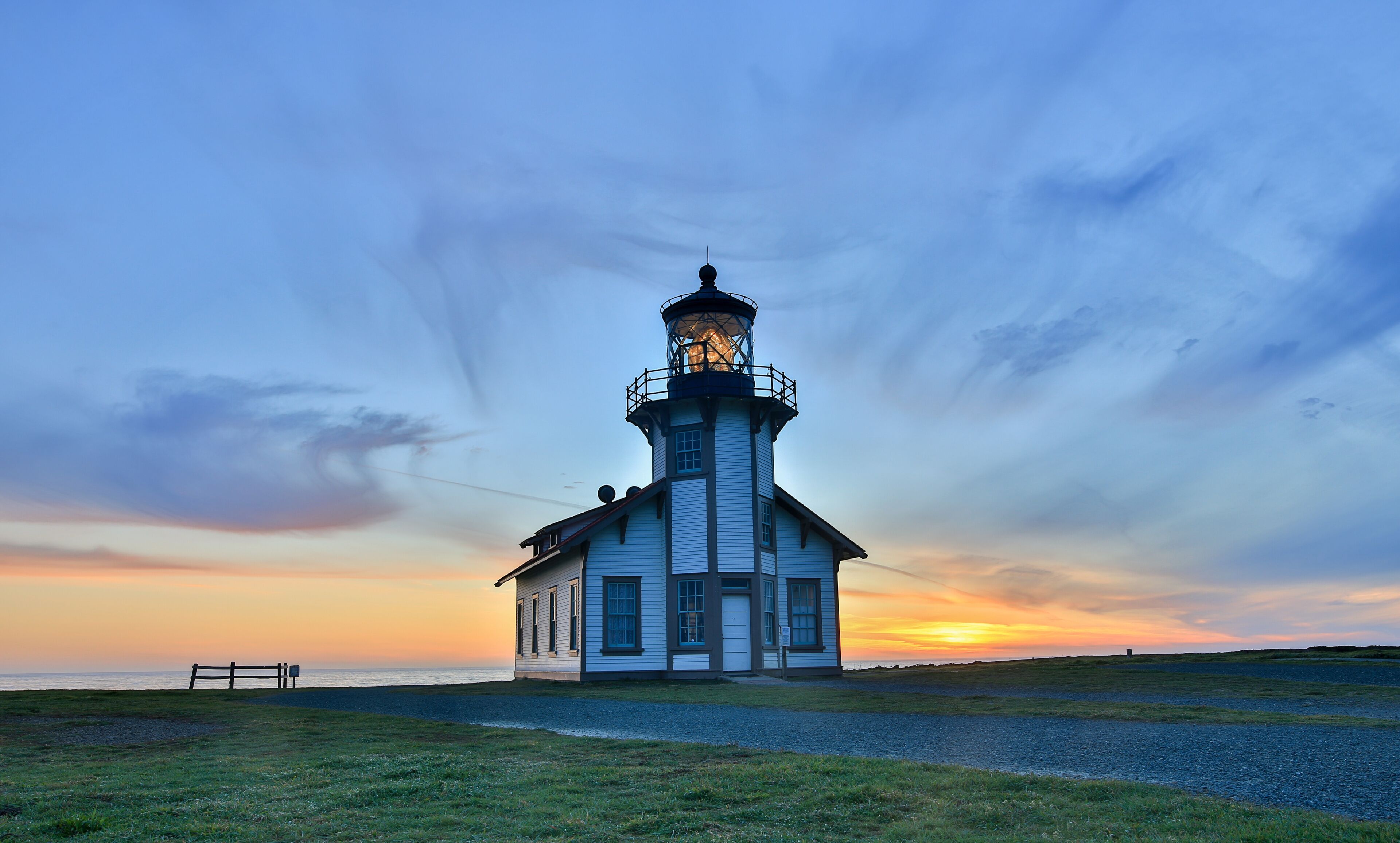 Un phare au coucher du soleil, avec un ciel dégagé et un banc à proximité.