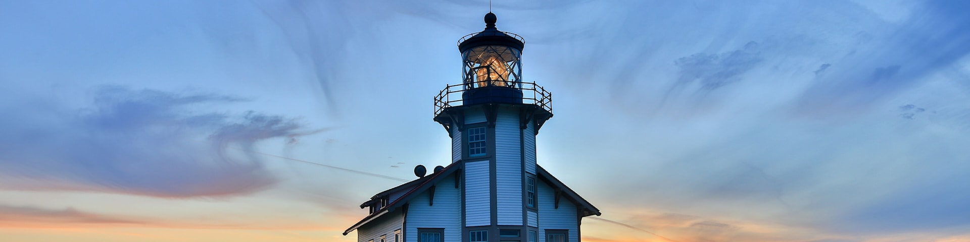 Un faro al atardecer, con cielo despejado y una banca cerca.