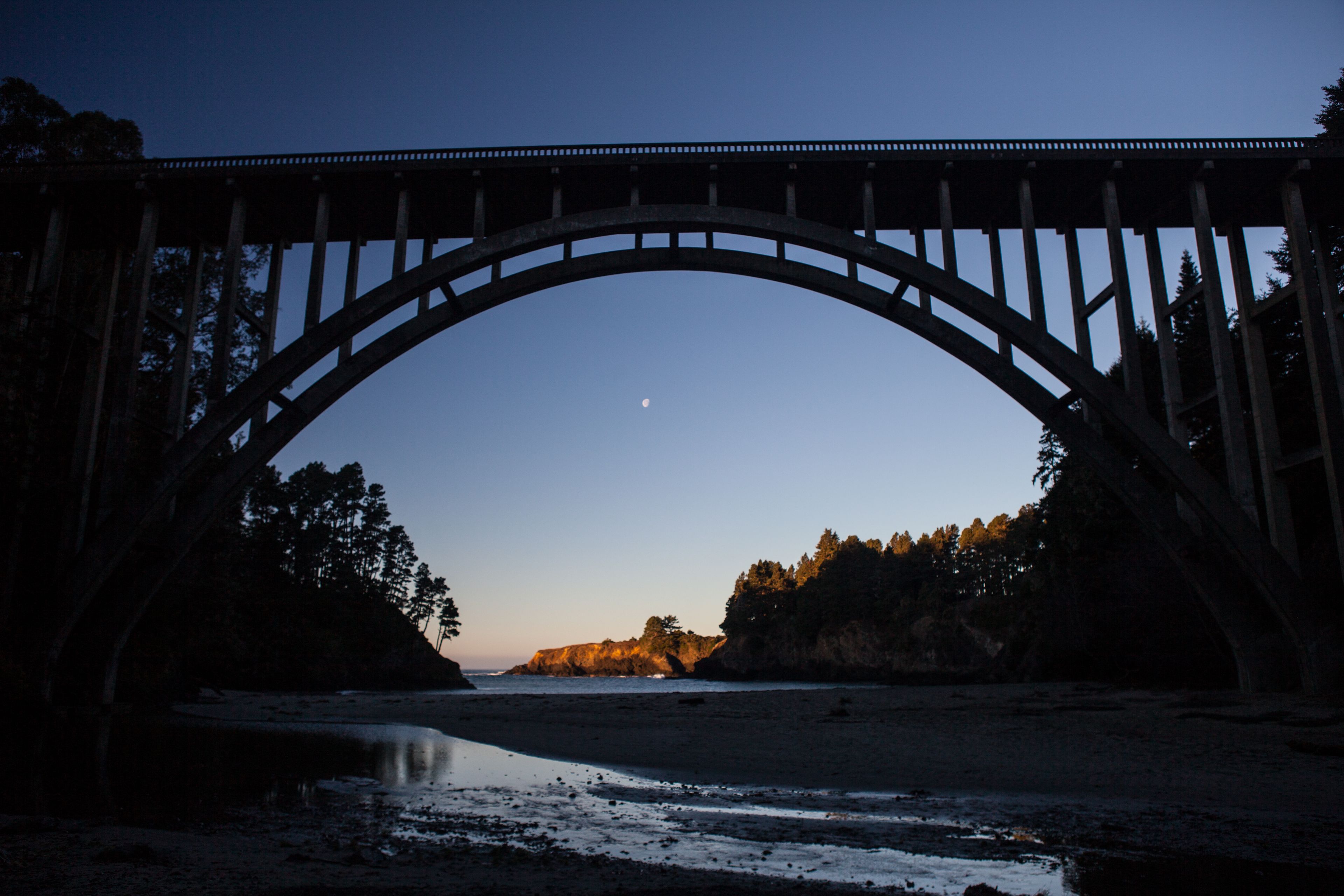 A bridge arching over a river with a moon in the sky.