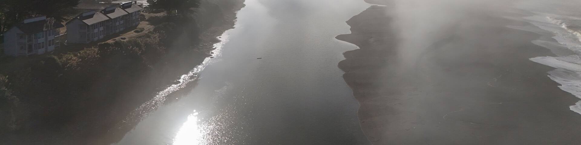 Aerial view of serene coastal fog over a tranquil river and lush trees, Gualala, California, United States.