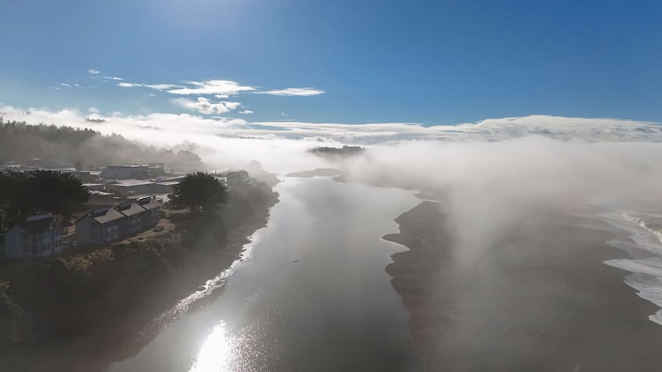 A coastal town with buildings near the shore, surrounded by fog and mist.