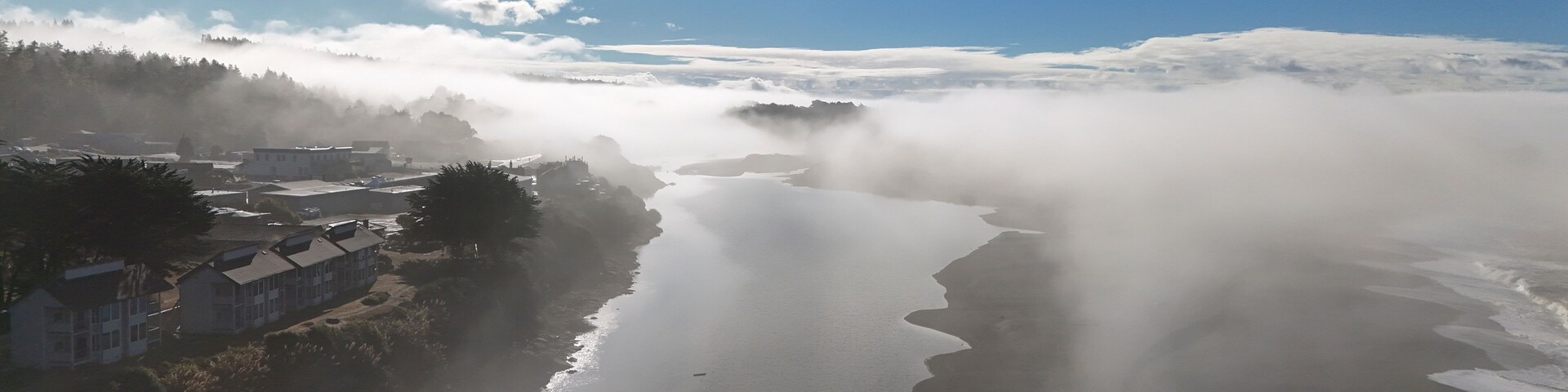 Aerial view of serene coastal fog over a tranquil river and lush trees, Gualala, California, United States.