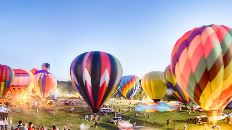 A hot air balloon festival with colorful balloons and a grassy field.