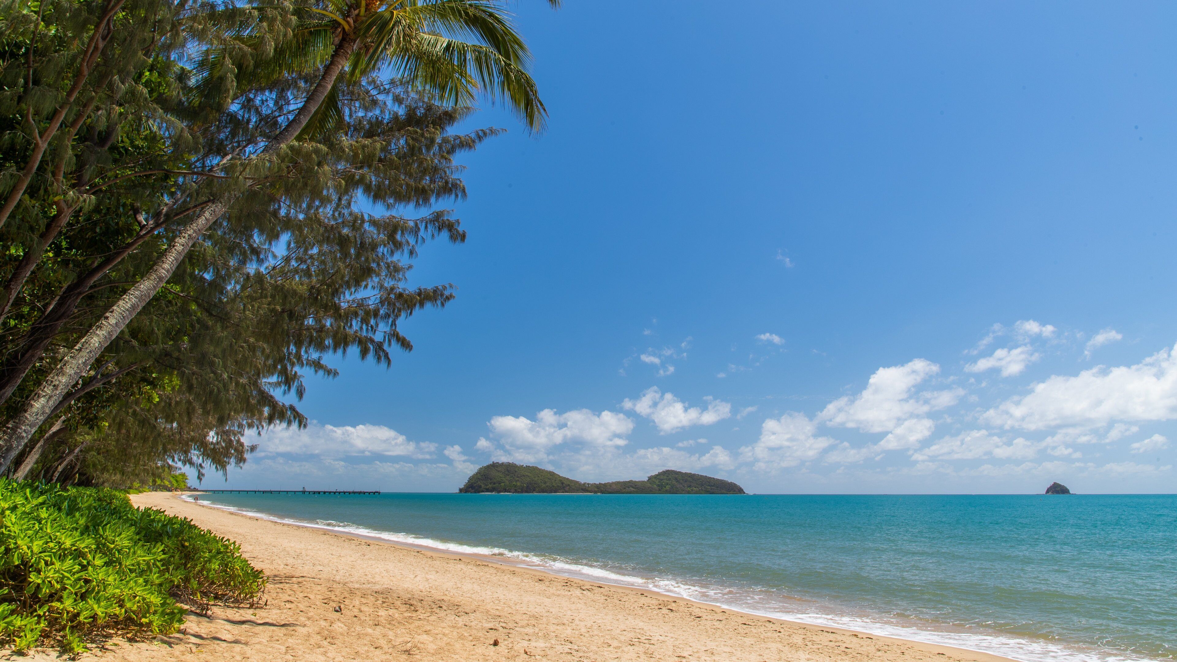 Une plage à l’eau turquoise et limpide, un rivage sablonneux et une île qui se dessine à l’horizon.