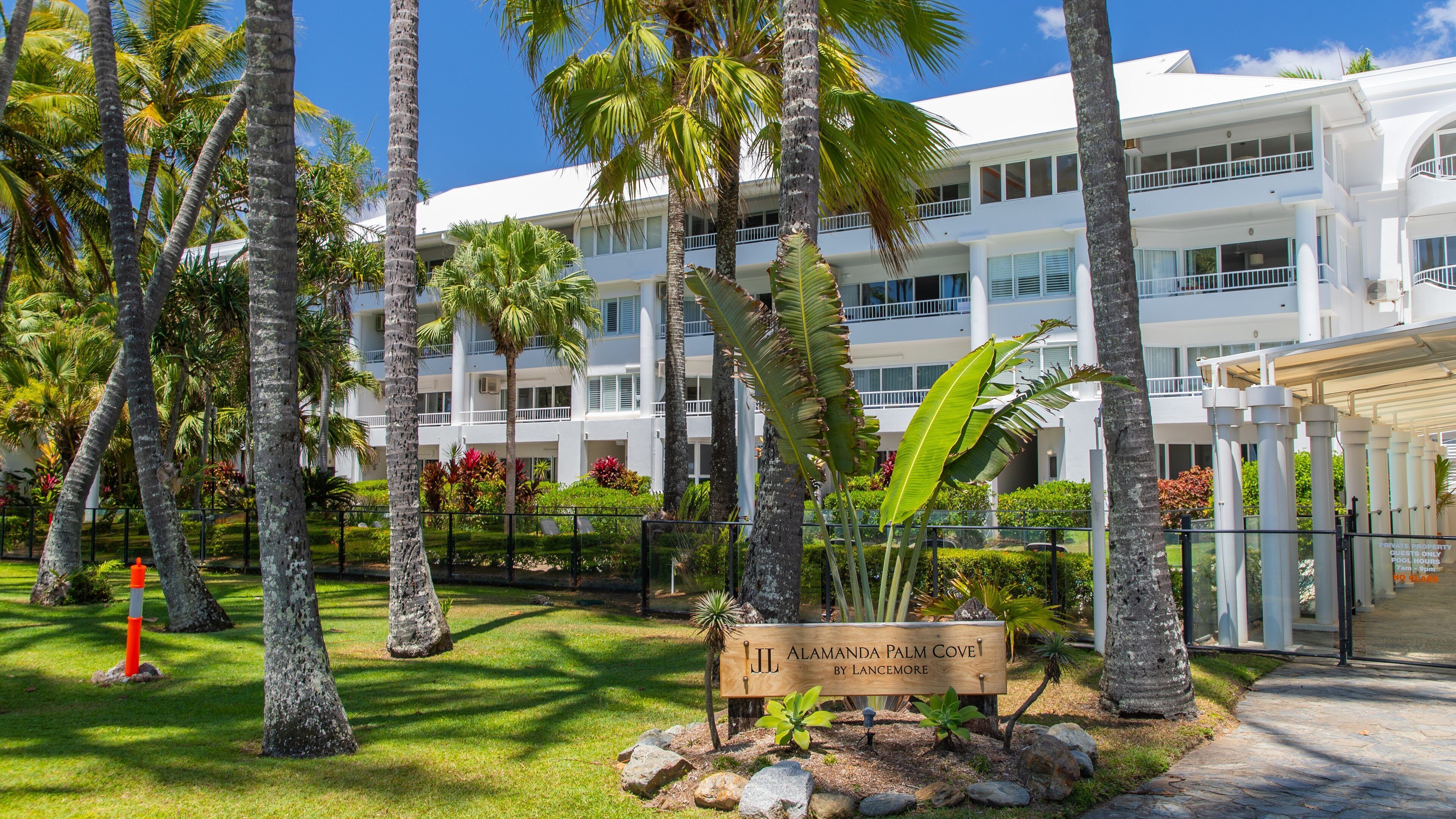 A resort with palm trees, a sign reading "Alamanda Palm Cove by Lancimore," and a white building with balconies.
