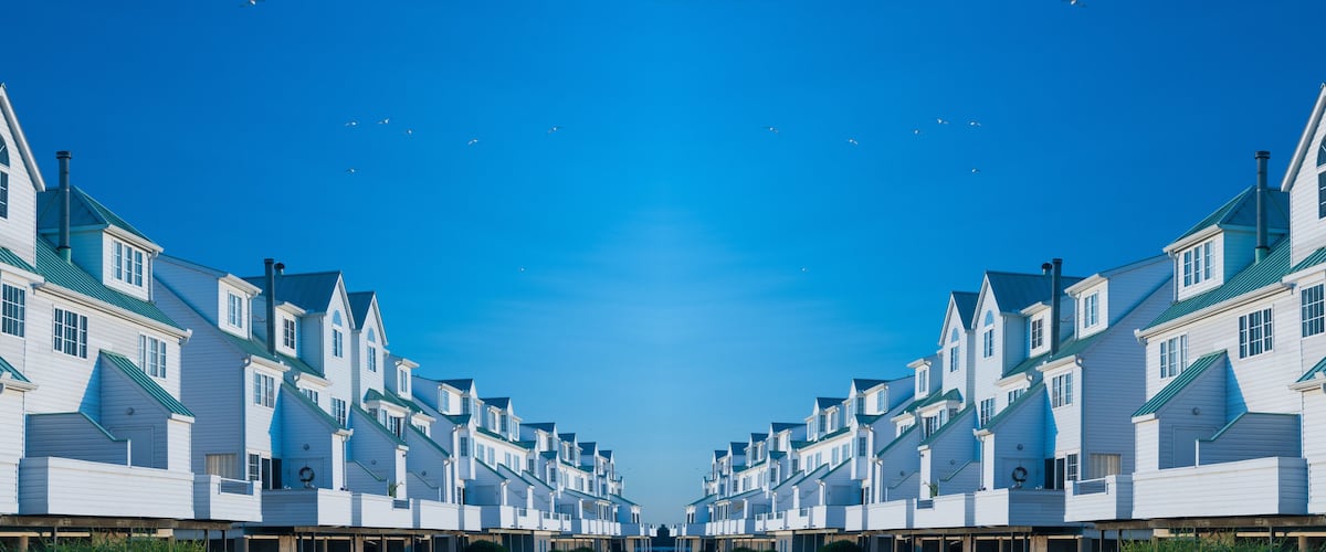 A symmetrical row of white houses with green roofs and chimneys under a clear blue sky.