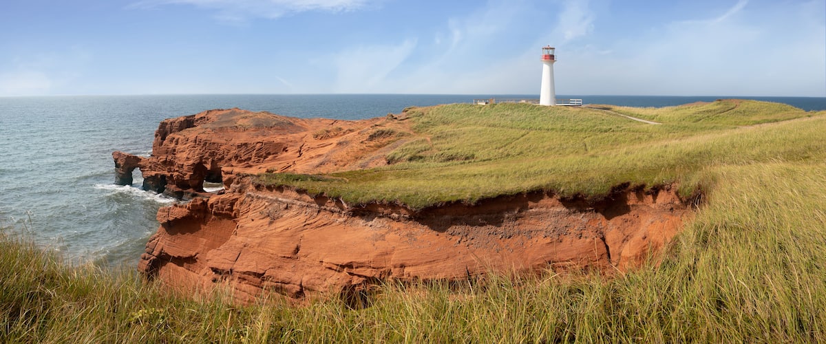 A lighthouse on a grassy cliff by the sea.