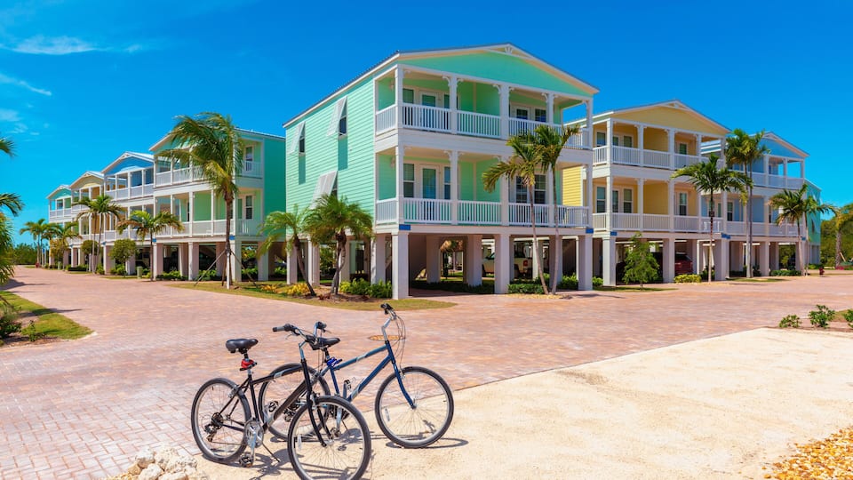 A multi-story resort with colorful buildings, a paved walkway, and palm trees.