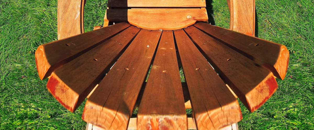 A wooden Adirondack chair facing a lake with a dock and a boat.
