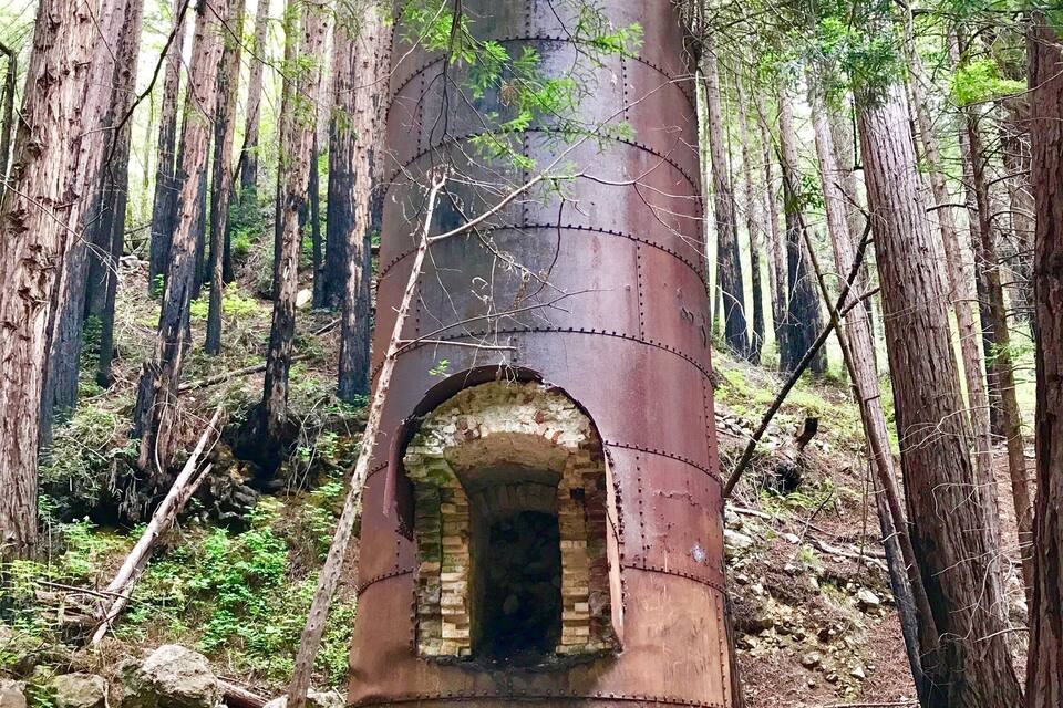Eine verrostete, zylindrische Struktur mit Bogenöffnung im Wald.