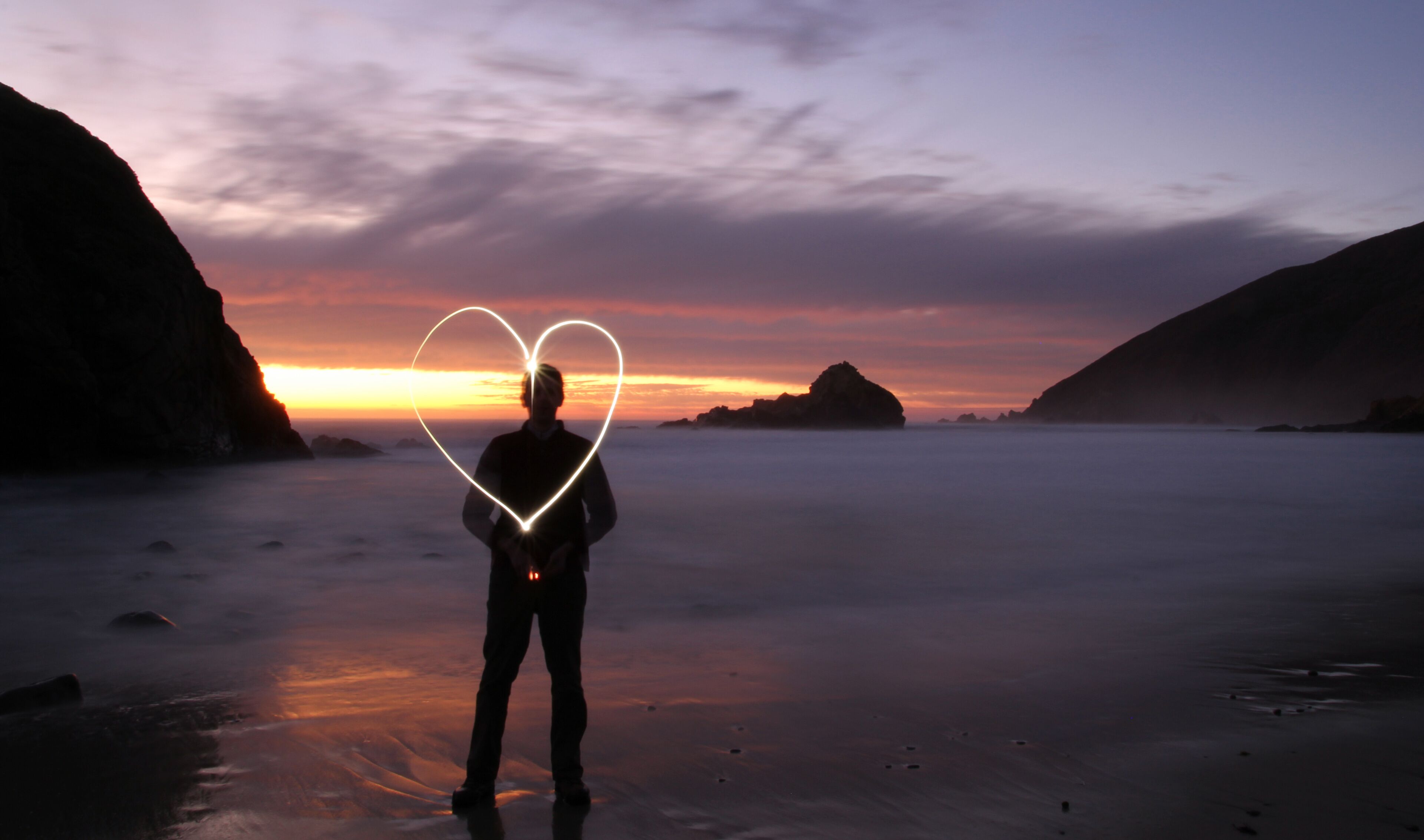 Man makes a loving heart light painting on the beach in Big Sur, California during sunset