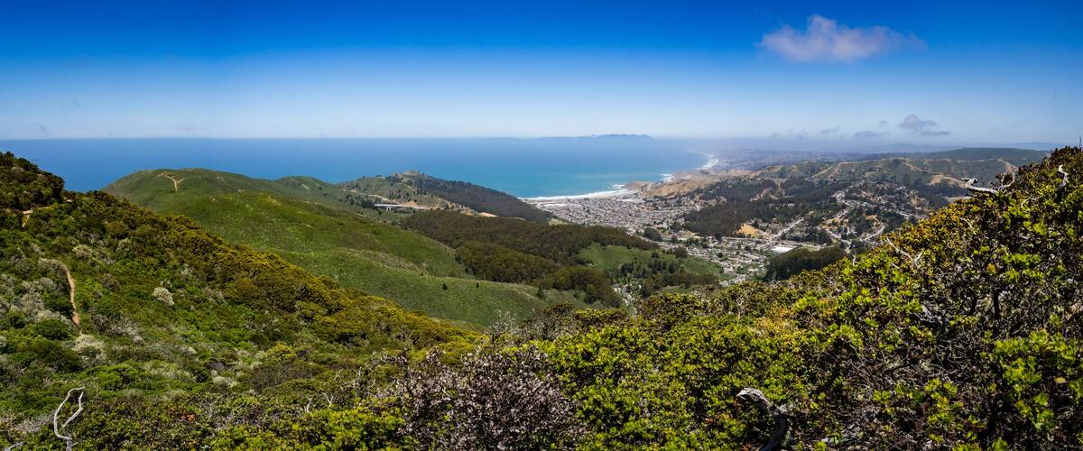 A coastal landscape with green hills, a beach, and a town in the distance.