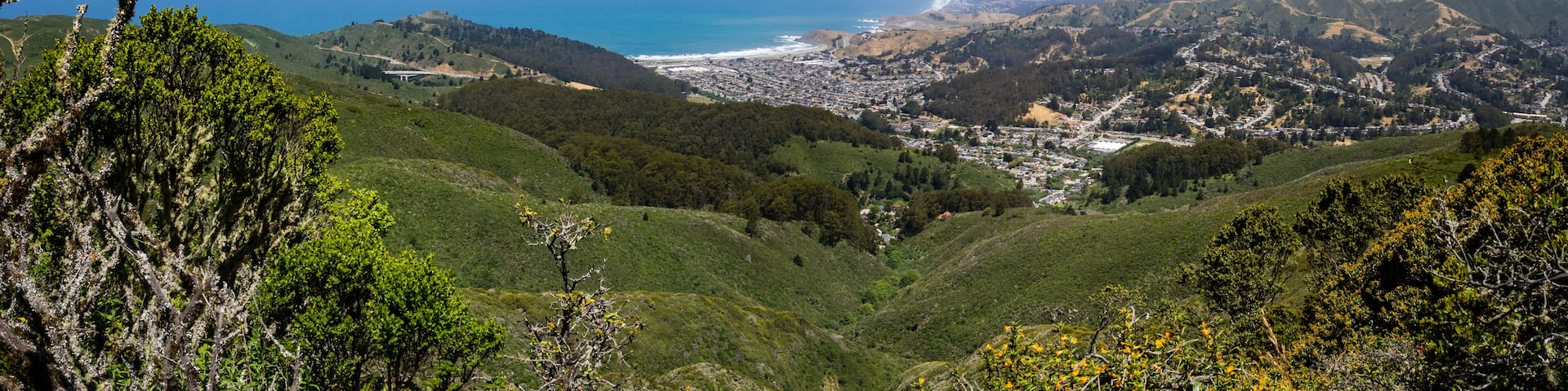 A coastal town nestled in a valley with a view of the ocean and rolling hills.