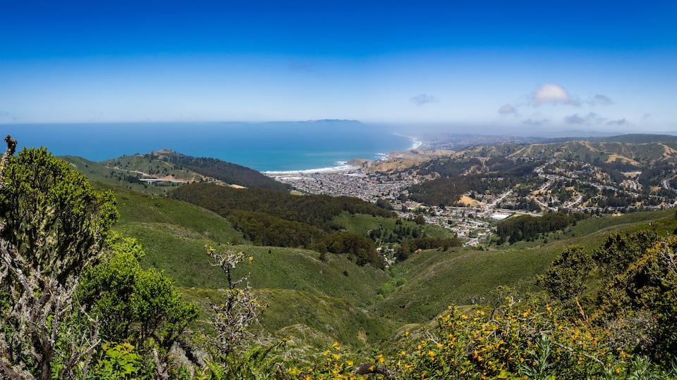 A coastal town nestled in a valley with a view of the ocean and rolling hills.