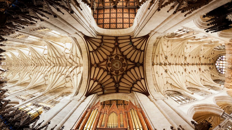 A cathedral interior with intricate ribbed vaults, a large organ, and stained glass windows.